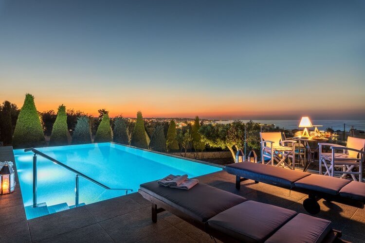 Swimming pool at sunset and two sun loungers, with coastal lights in the background