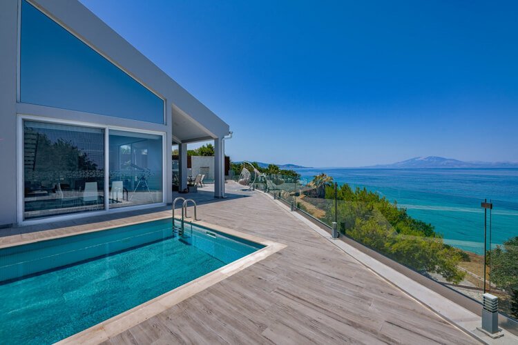 Villa, swimming pool, wooden deck surrounded by glass barriers with sea and islands in the distance 