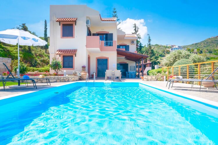 White and pink villas with hills in the background and a large pool in the foreground