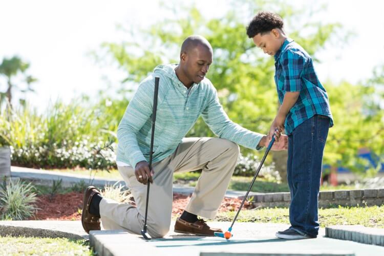 My father teaches his son how to play mini golf.