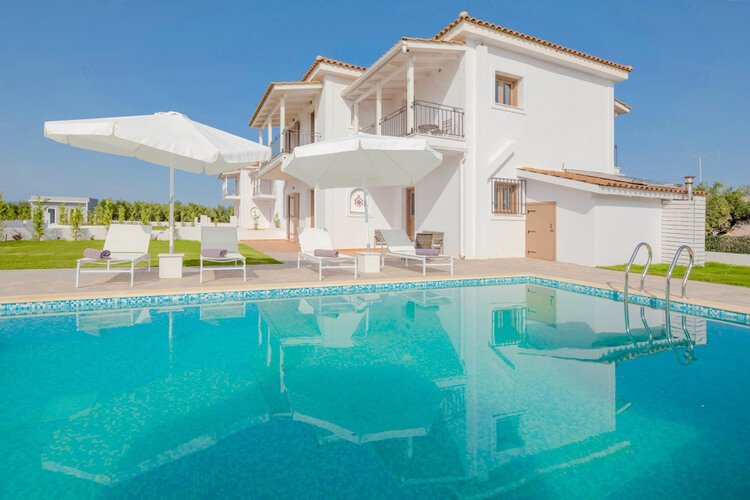 White villa with tan tiles and doors, with a large pool in the foreground