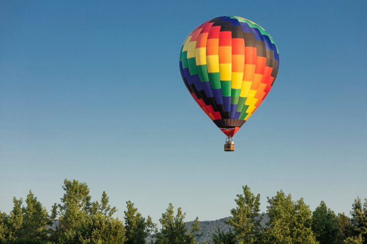 A colorful hot air balloon floating on some trees.