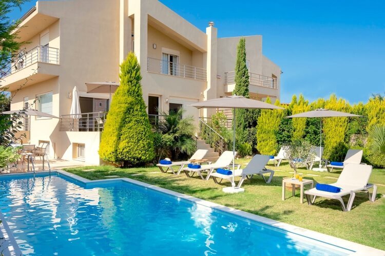 White villa with several terraces on blue background, pool and some sun loungers in the foreground