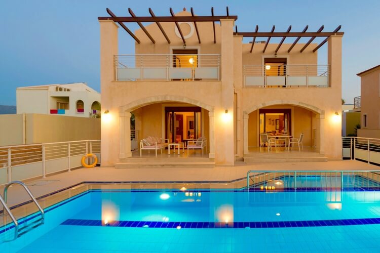 An orange villa with a wooden cover on the balcony and a bright blue pool in the foreground