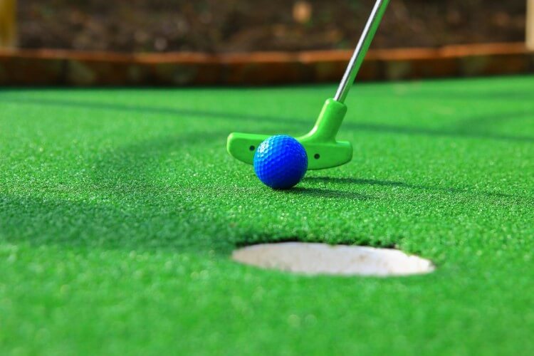 A green golf club that puts a blue golf ball in a hole.